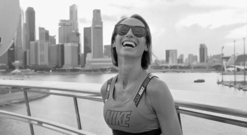 Francesca Leighton laughing on a waterfront walkway, a city skyline behind her.